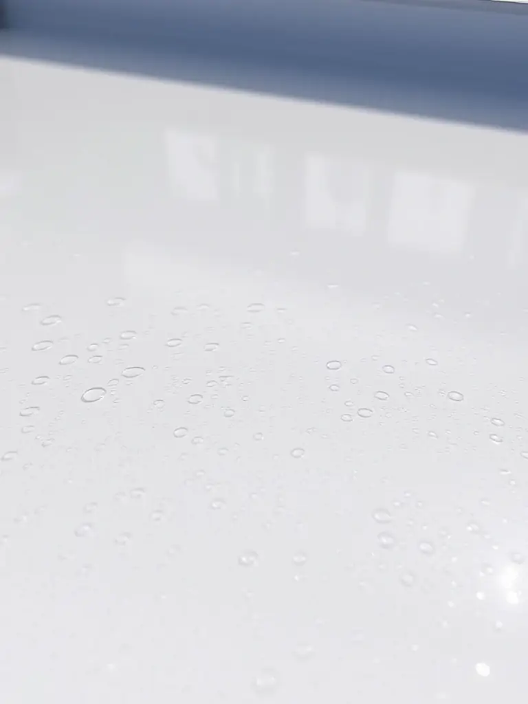 A close-up shot of a can of NABER Premium Waterproofing Coating, showcasing its label and texture, with water droplets beading on the surface to emphasize its waterproof properties. The background is a construction site.